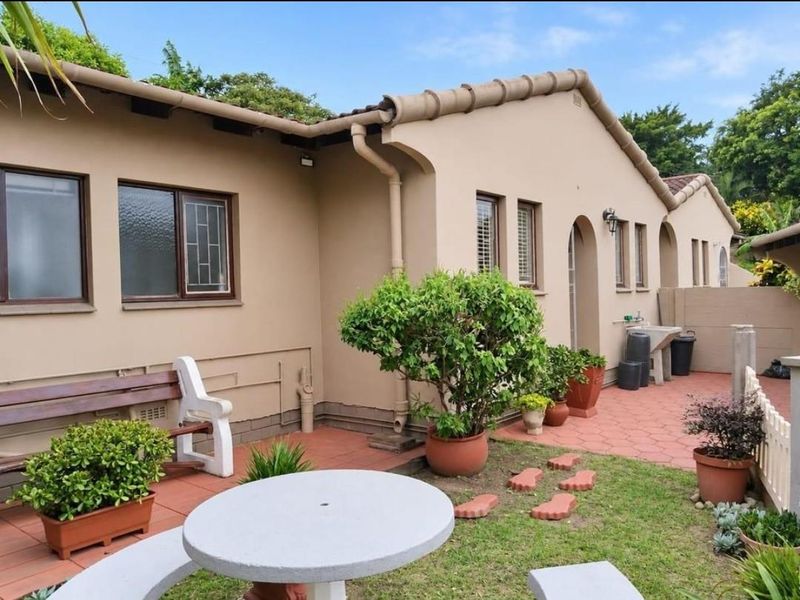 A rear exterior view of the townhouse featuring a paved patio area, garden space, and functional outdoor utility sink.