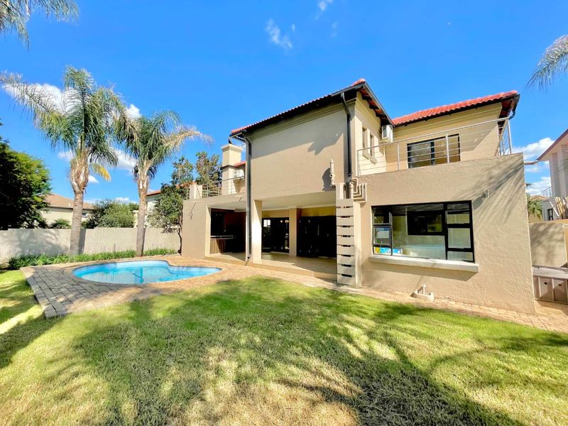 Rear view of the property featuring a swimming pool, paved patio area, built-in braai, and an upper-level balcony.