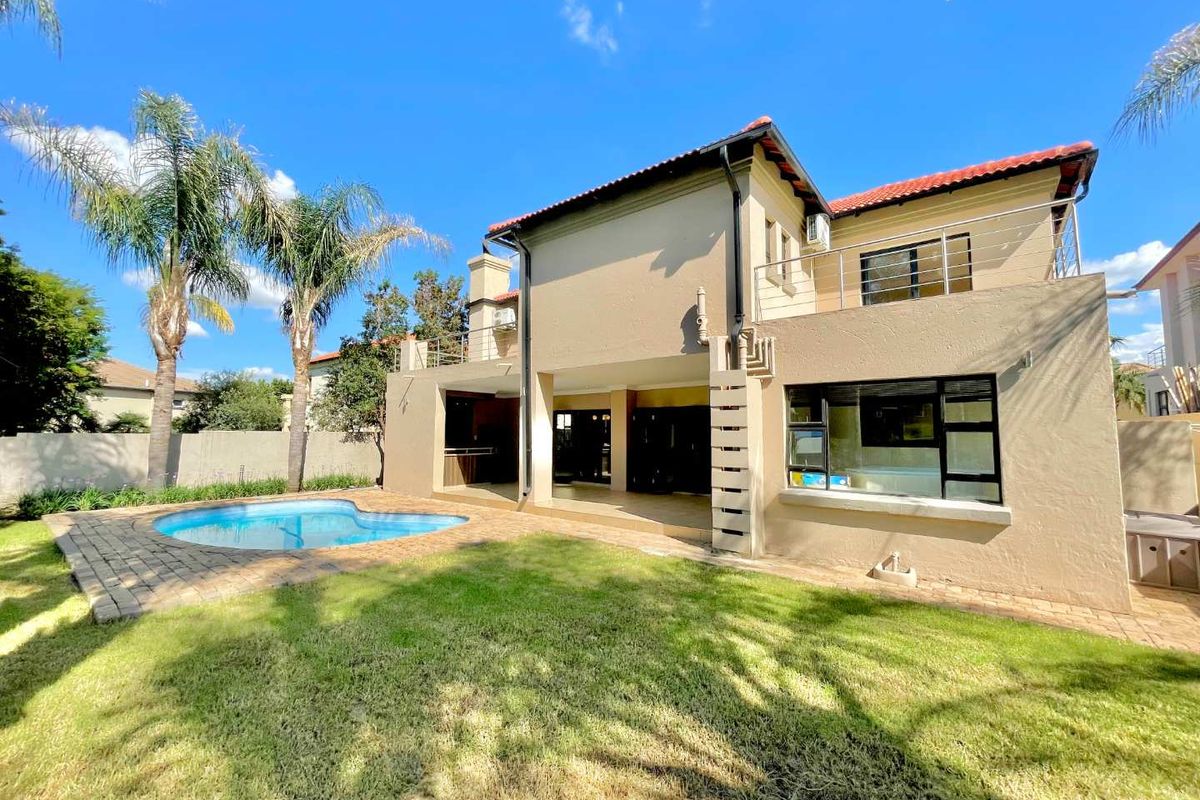 Rear view of the property featuring a swimming pool, paved patio area, built-in braai, and an upper-level balcony.