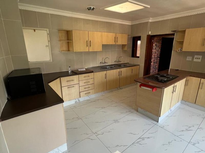Spacious kitchen featuring light wood cabinetry, dark countertops, a built-in gas hob, and large marble-look floor tiles.