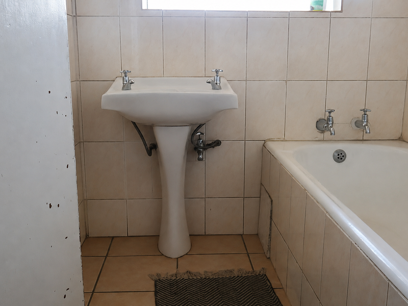 A functional bathroom featuring a pedestal basin, built-in bathtub, and neutral ceramic tiling throughout, offering a clean and simple layout.
