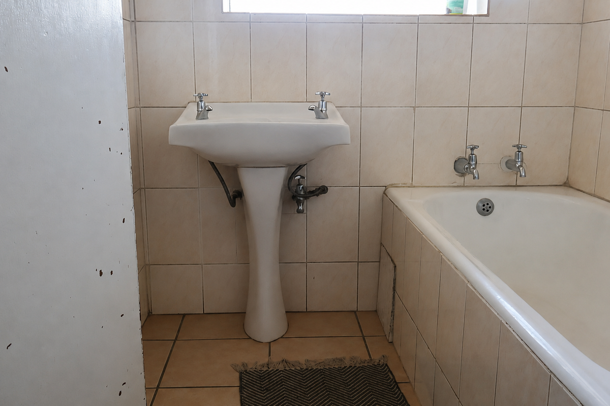 A functional bathroom featuring a pedestal basin, built-in bathtub, and neutral ceramic tiling throughout, offering a clean and simple layout.