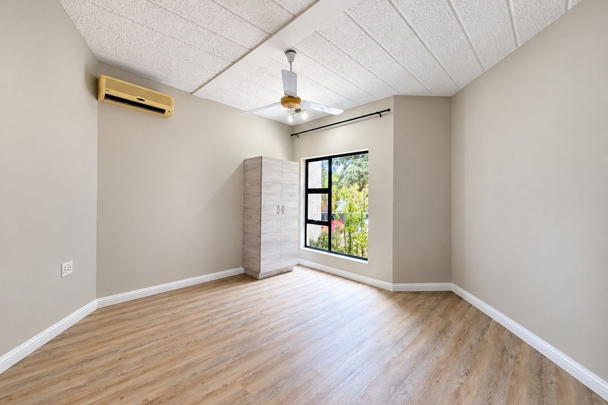 A bright, empty bedroom featuring modern laminate flooring, a ceiling fan, and a built-in wardrobe, offering a clean and neutral space ready for personalization.