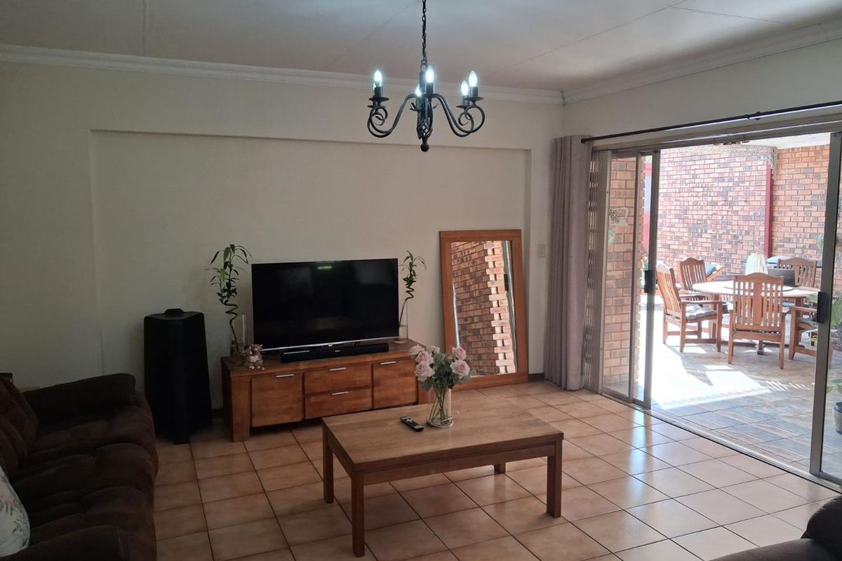 A spacious living room featuring tiled flooring, a decorative chandelier, and large sliding glass doors that open onto a private brick-walled patio area.
