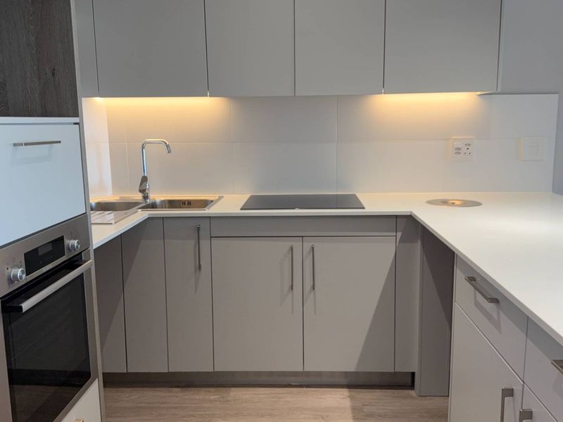 Modern kitchen featuring sleek grey cabinetry, quartz countertops, integrated oven, induction hob, and under-cabinet lighting in a clean, contemporary finish.
