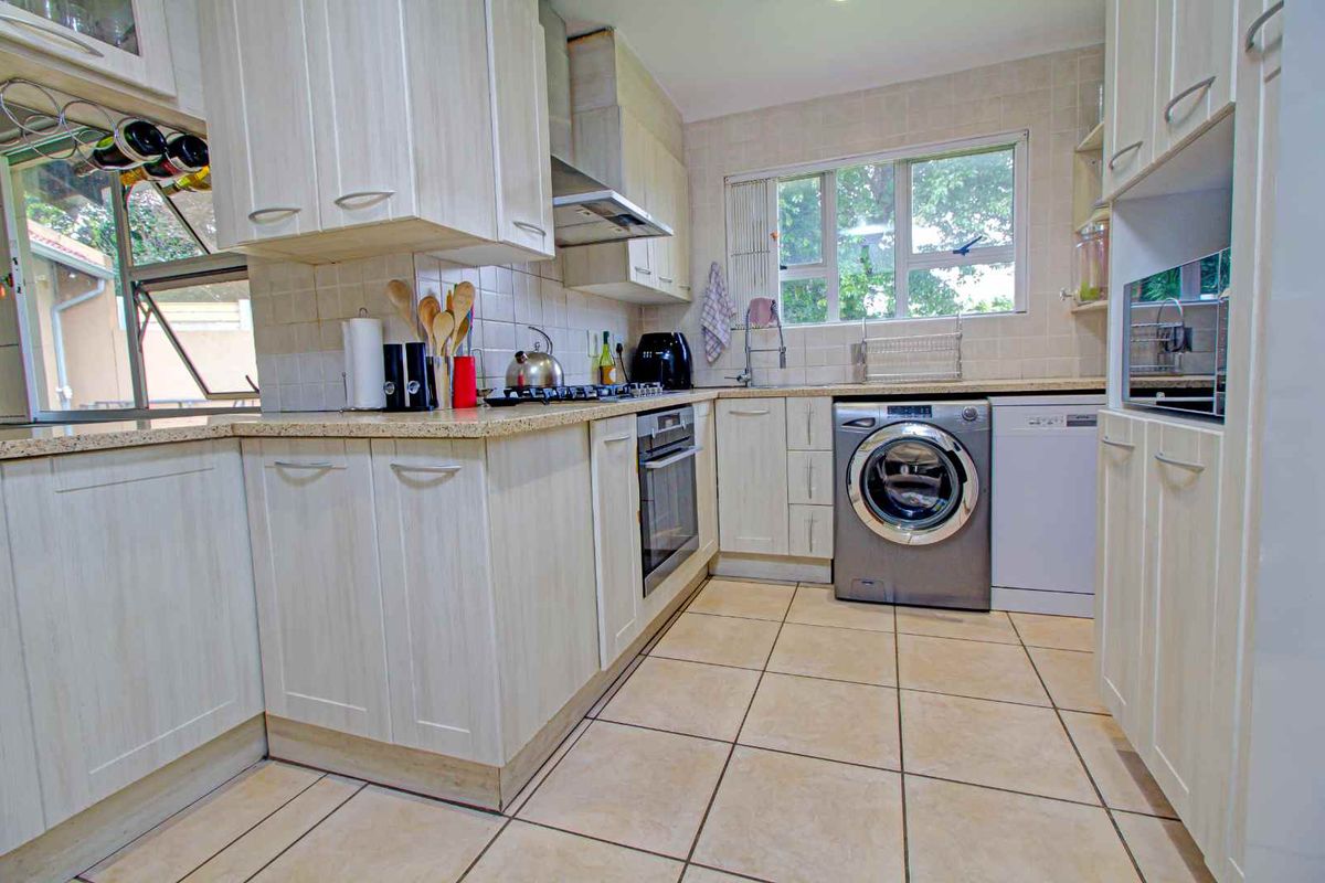 A functional kitchen featuring light-toned cabinetry, tiled flooring, a built-in oven, gas hob, extractor fan, and integrated laundry and dishwasher plumbing.