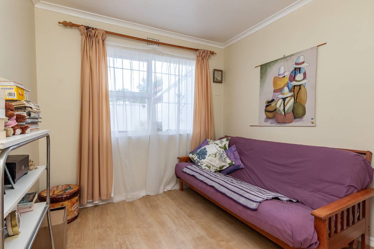 A bedroom featuring light-toned laminate flooring, neutral wall finishes, and a window fitted with security bars.
