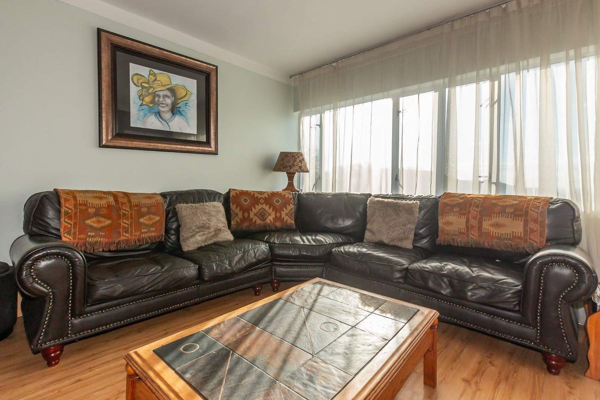 A comfortable living room featuring laminate flooring and large windows with sheer curtains, providing ample natural light.