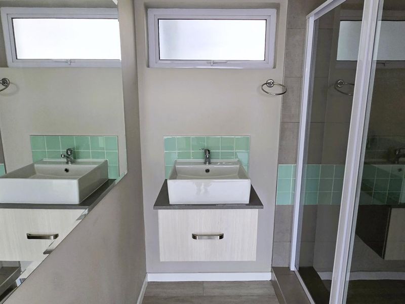 A clean, modern bathroom featuring a vessel sink with vanity cabinet, a shower enclosure, and light-toned tiled splashbacks.