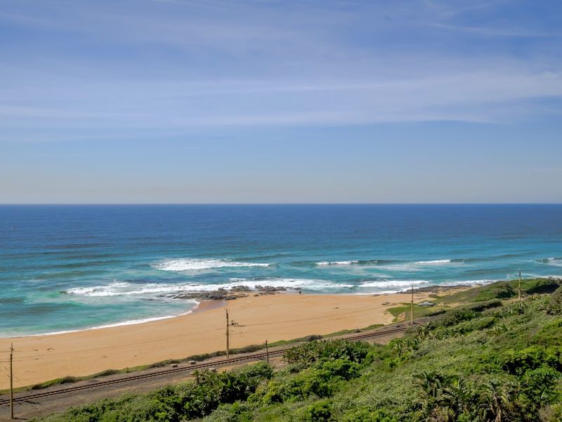 A scenic coastal view overlooking the sandy beach, ocean waves, and nearby railway tracks.