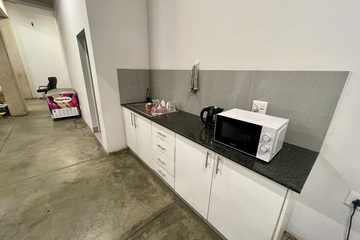 A functional kitchenette area featuring white cabinetry, a dark stone countertop, and a tiled splashback, situated within an industrial warehouse space.