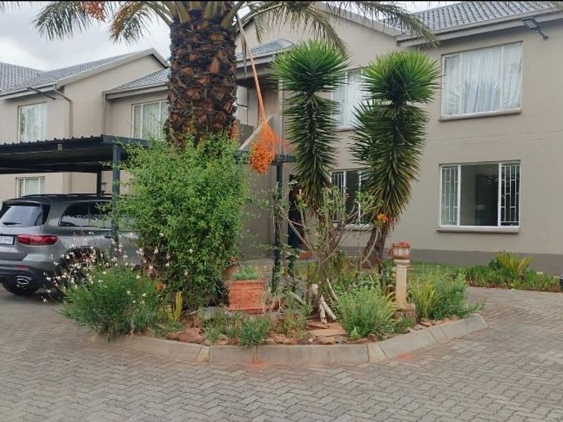 Front exterior view of a townhouse complex featuring a paved driveway, covered carport parking, and established garden landscaping.
