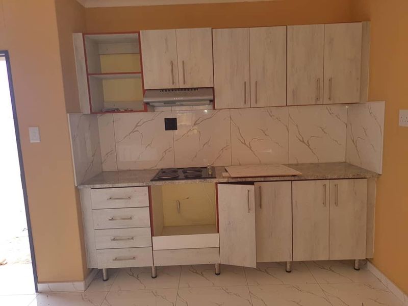 A compact kitchen featuring light wood-grain cabinetry, marble-look splashback tiles, and a built-in hob with an extractor fan.