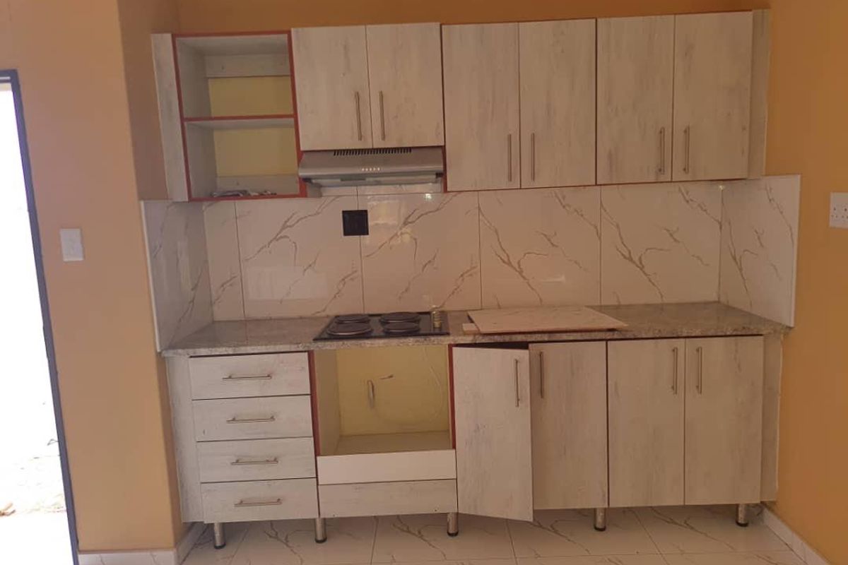 A compact kitchen featuring light wood-grain cabinetry, marble-look splashback tiles, and a built-in hob with an extractor fan.