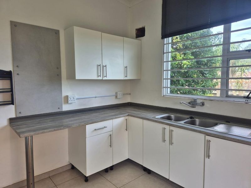 A functional kitchen area featuring white cabinetry, laminate countertops, a double stainless steel sink, and tiled flooring, ready for personalization.