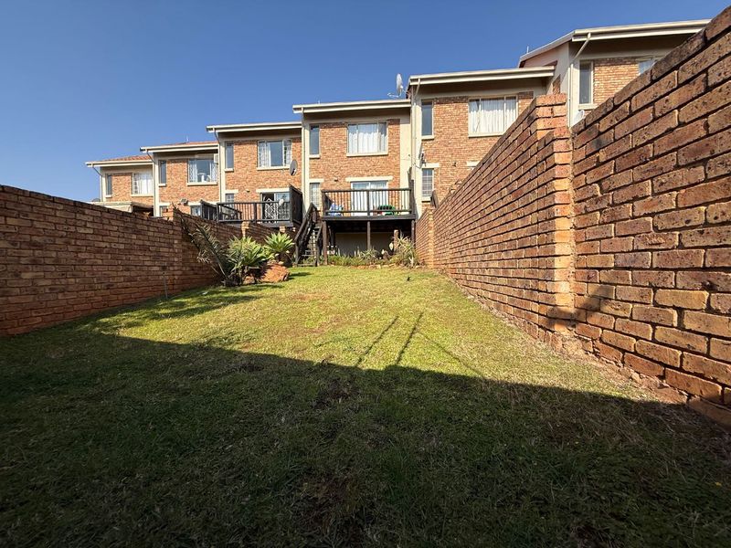 A rear view of the townhouse featuring a private lawn area enclosed by brick boundary walls and an elevated timber deck.