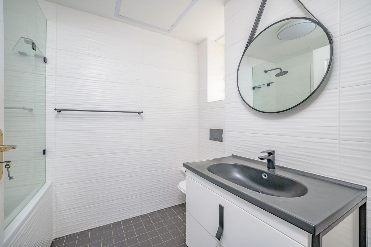 Modern bathroom featuring a sleek vanity with integrated sink, glass shower screen, bathtub, and contemporary black fixtures against textured white wall tiles.