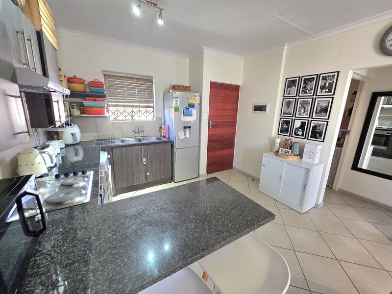 A functional kitchen featuring granite countertops, built-in cabinetry, a hob with extractor fan, and tiled flooring, providing a practical workspace.