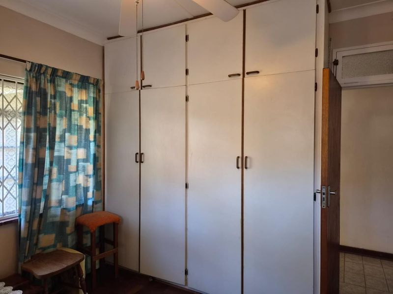 A bedroom featuring floor-to-ceiling built-in cupboards, a ceiling fan, and a security gate on the window.
