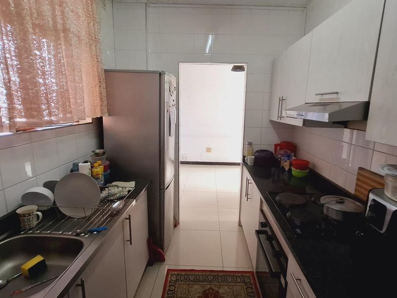 A functional galley-style kitchen featuring built-in cabinetry, a stainless steel sink, electric hob, oven, and extractor fan with tiled finishes.