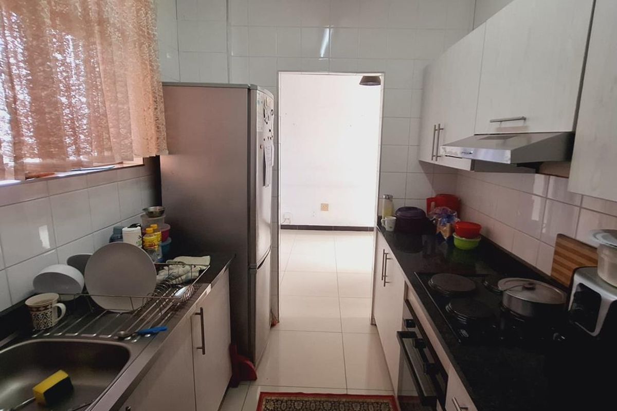 A functional galley-style kitchen featuring built-in cabinetry, a stainless steel sink, electric hob, oven, and extractor fan with tiled finishes.