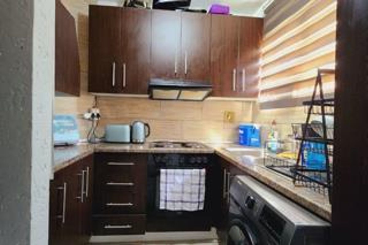 Compact kitchen featuring dark wood cabinetry, integrated oven and hob, extractor fan, and tiled backsplash with a functional layout.