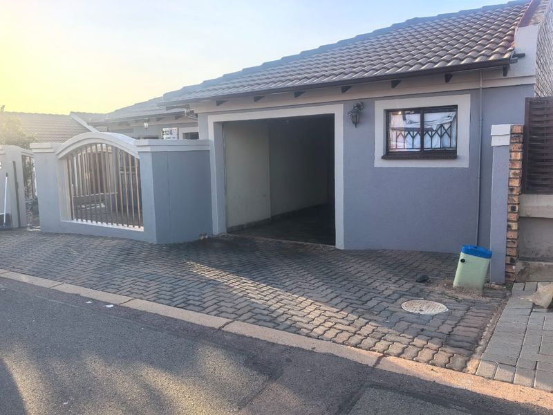 Front exterior view of the property featuring a paved driveway, a single garage entrance, and a secure perimeter wall with metal gate.