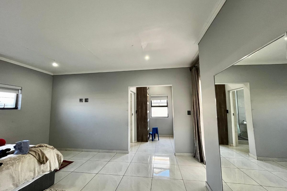 Spacious bedroom featuring large format floor tiles, neutral grey walls, and an adjoining dressing area leading to an en-suite bathroom.