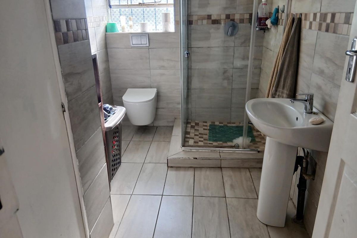 A functional bathroom featuring a glass-enclosed shower, wall-mounted toilet, and a pedestal basin with neutral wall and floor tiling.