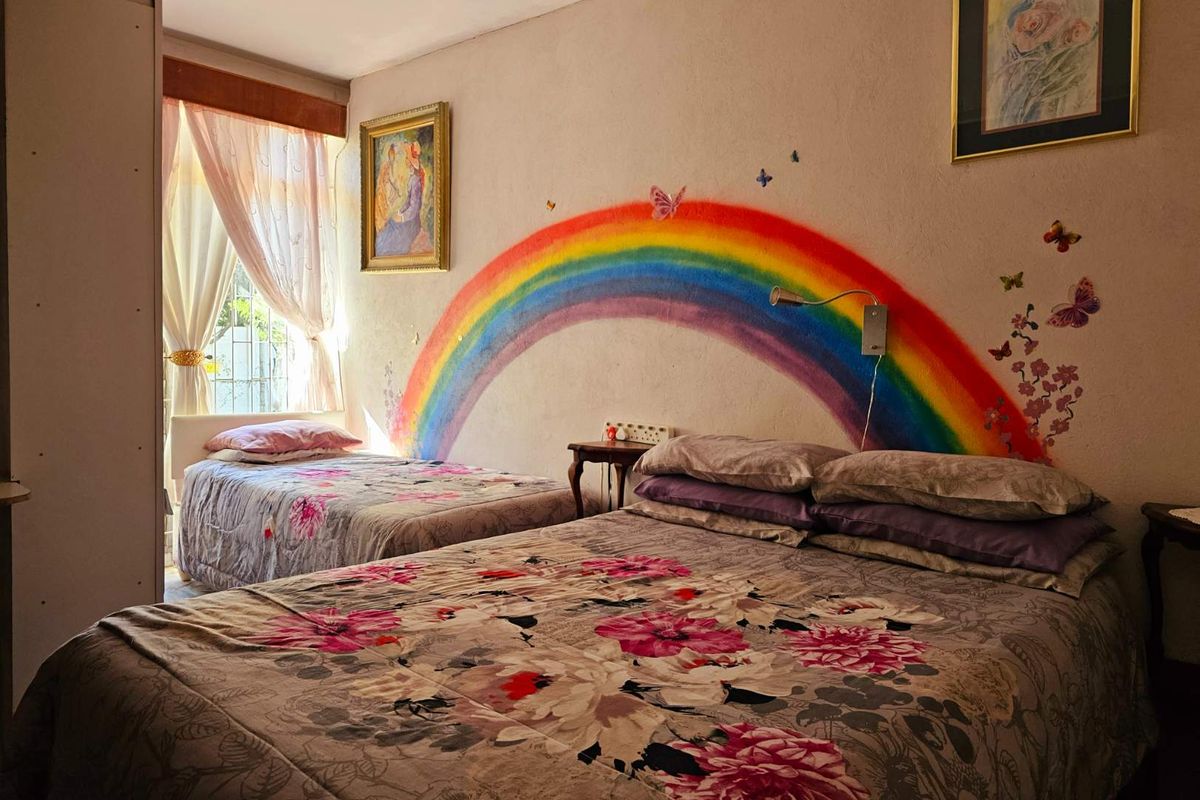 A bedroom featuring a painted rainbow mural on the wall, natural light from a window, and space for multiple beds.