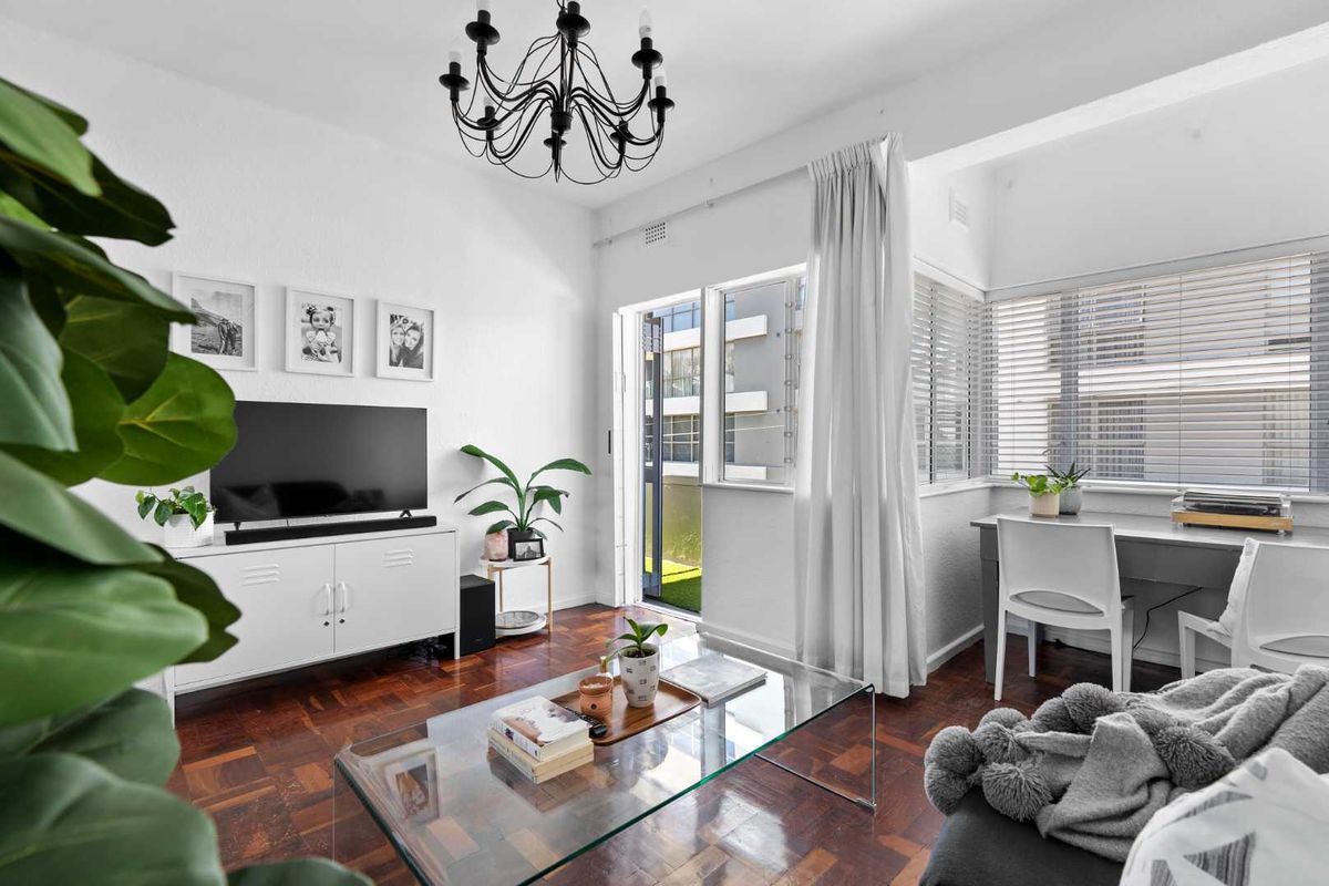 Bright living room featuring classic parquet flooring, a decorative chandelier, and large windows providing natural light with access to an outdoor area.
