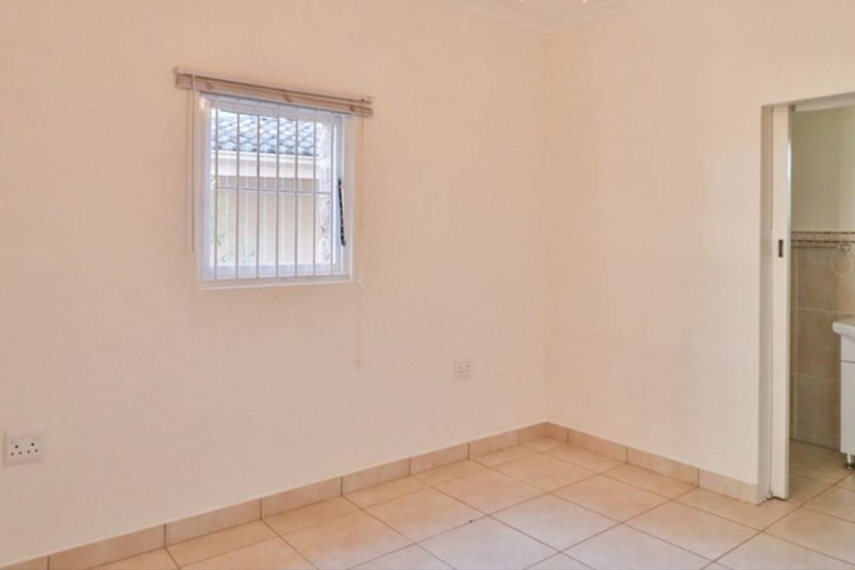 An empty bedroom featuring tiled flooring, security bars on the window, and an adjoining en-suite bathroom with a vanity basin.