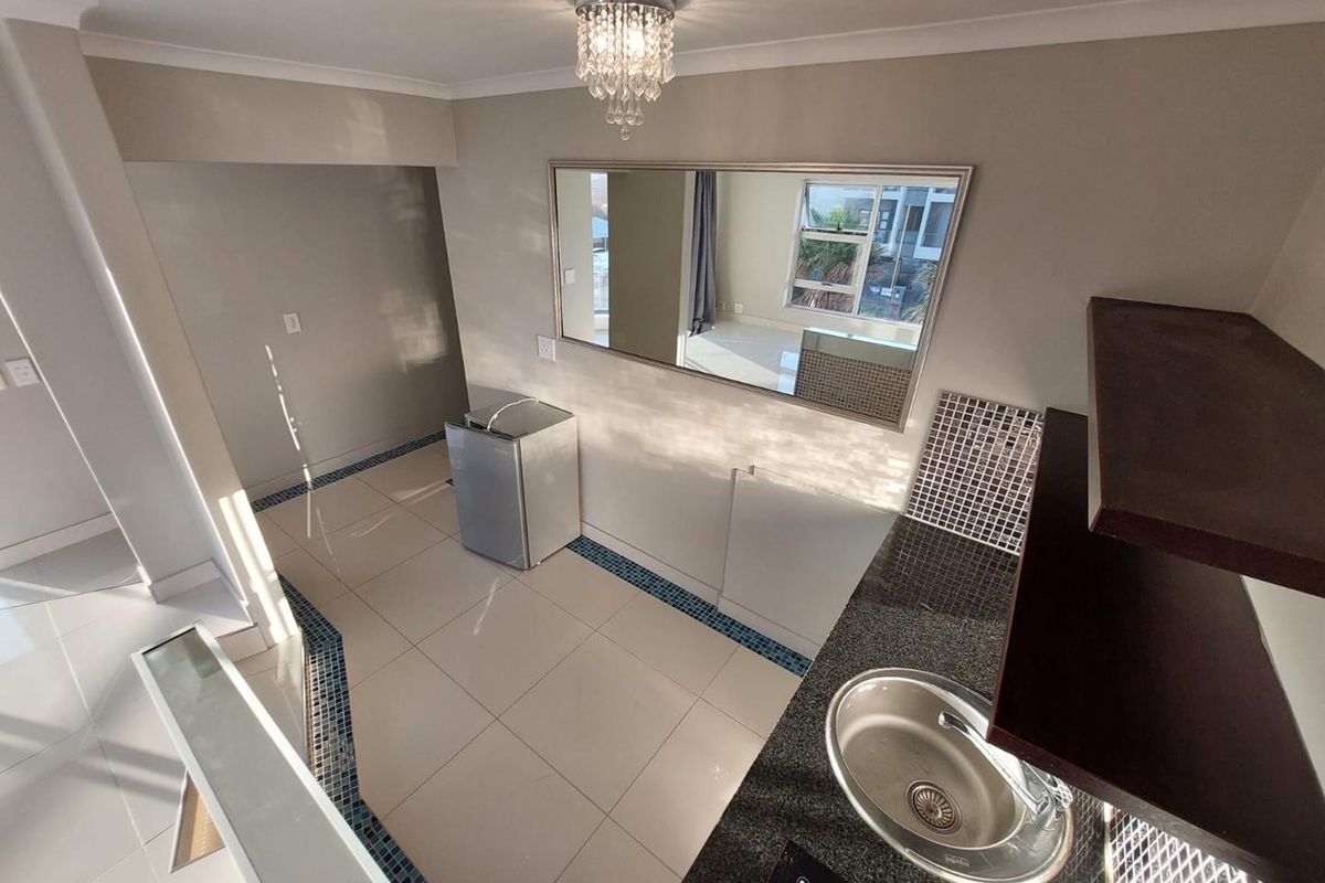 A compact kitchen area featuring granite countertops, a stainless steel sink, mosaic tile accents, and polished ceramic flooring with a modern crystal light fixture.