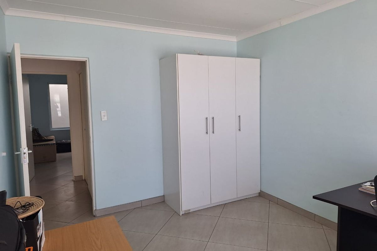 A bedroom featuring tiled flooring, a built-in wardrobe, and neutral wall finishes, offering a functional space with direct access to the hallway.