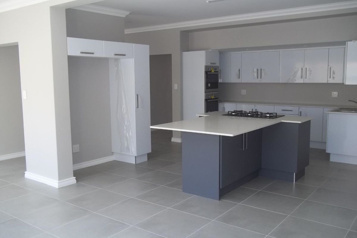 Modern open-plan kitchen featuring a central island with a gas hob, built-in oven, sleek cabinetry, and neutral floor tiling throughout.