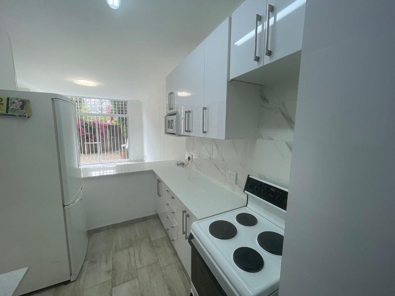 Modern kitchen featuring white gloss cabinetry, stone countertops, marble-look backsplash, and built-in appliances, with a bright window overlooking the exterior.