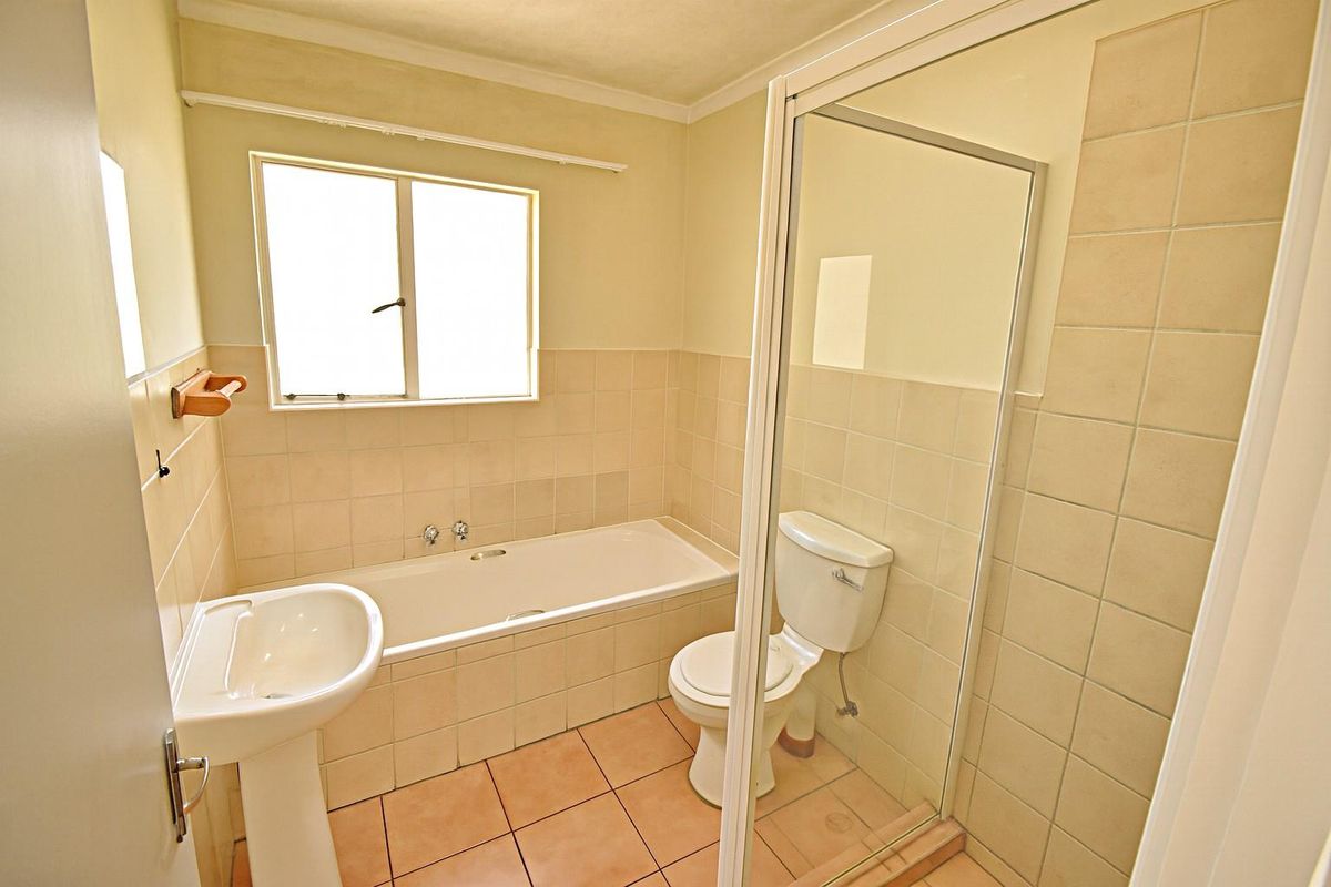 A functional bathroom featuring a pedestal basin, a built-in bathtub, and a separate glass-enclosed shower with neutral wall tiling.