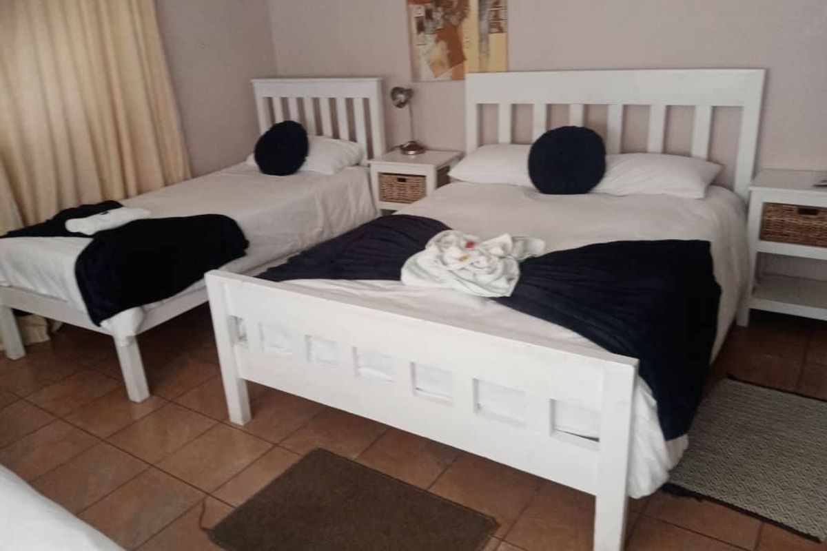 A guest bedroom featuring tiled flooring and neutral wall tones, configured with two white wooden bed frames.
