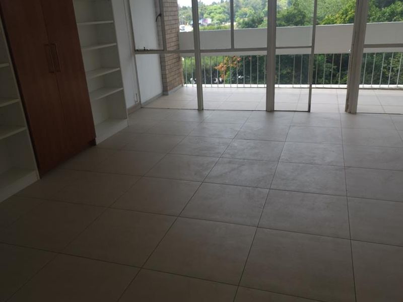 Spacious bedroom featuring neutral tiled flooring, built-in cupboards, and large glass sliding doors leading to a balcony with scenic views.