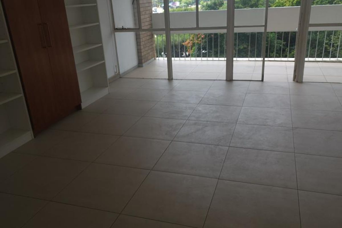 Spacious bedroom featuring neutral tiled flooring, built-in cupboards, and large glass sliding doors leading to a balcony with scenic views.