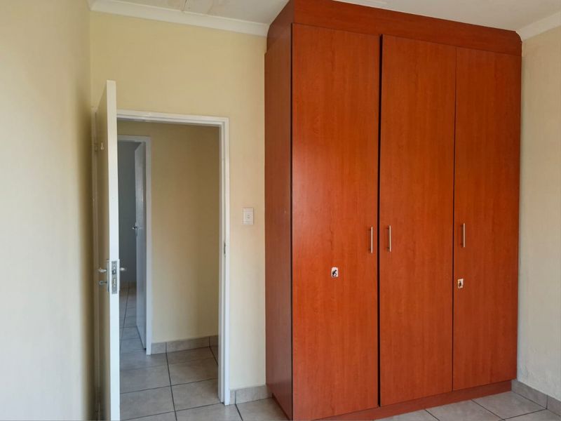 A bedroom featuring tiled flooring and a large built-in wooden wardrobe, offering a functional and neutral space ready for personalization.