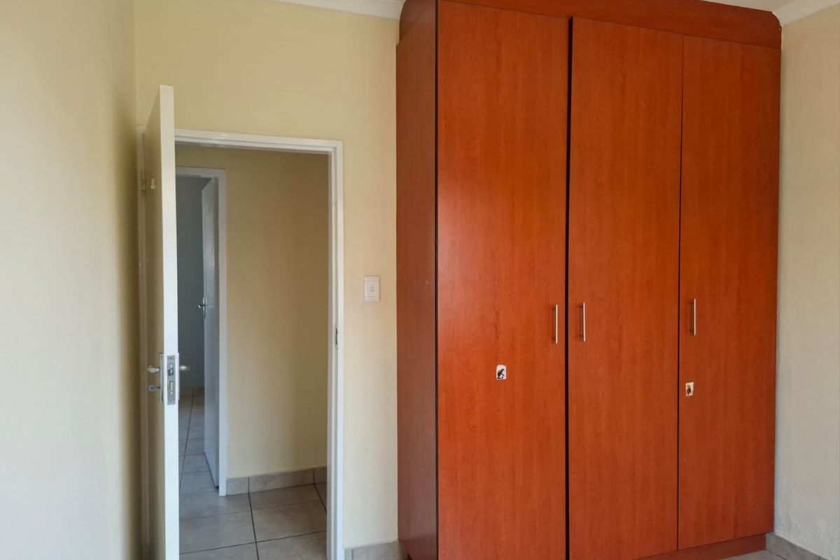 A bedroom featuring tiled flooring and a large built-in wooden wardrobe, offering a functional and neutral space ready for personalization.