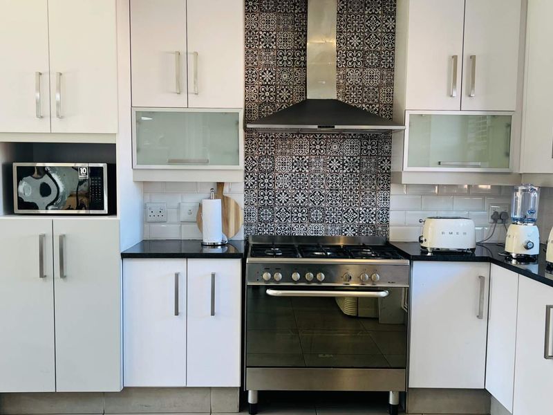 Modern kitchen featuring white cabinetry, granite countertops, a gas stove with a decorative patterned tile splashback, and integrated microwave.