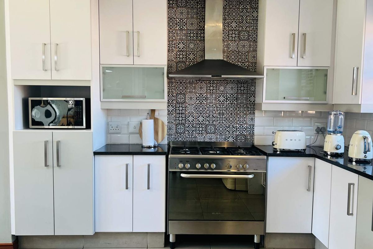 Modern kitchen featuring white cabinetry, granite countertops, a gas stove with a decorative patterned tile splashback, and integrated microwave.