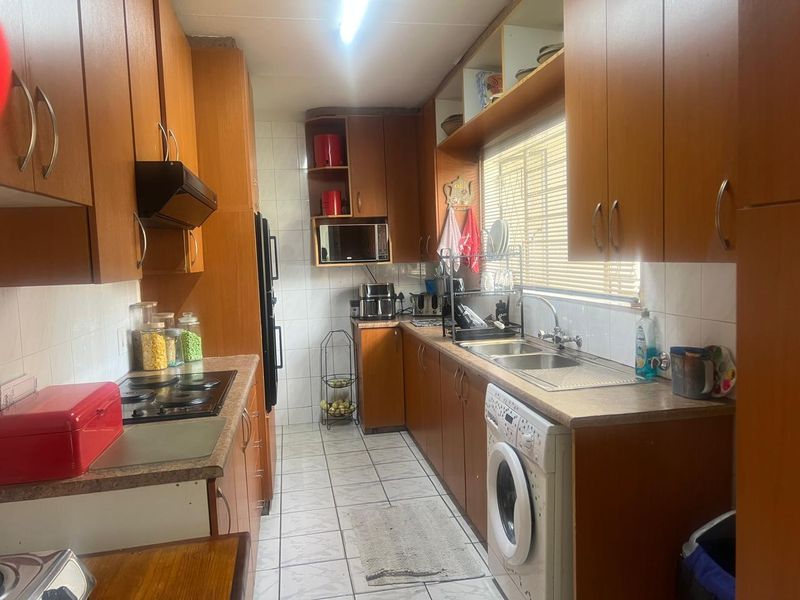 A functional galley-style kitchen featuring wood-look cabinetry, laminate countertops, an electric hob, and integrated laundry plumbing.