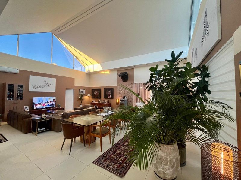 Spacious open-plan living and dining area featuring high vaulted ceilings, large triangular clerestory windows, and modern tiled flooring.