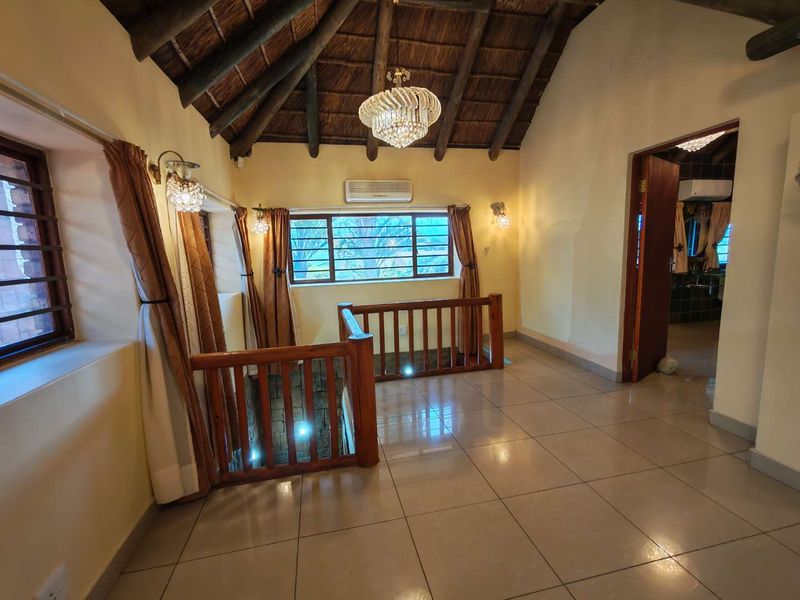 Spacious living area featuring a high vaulted thatched ceiling with exposed timber rafters, tiled flooring, and a timber balustrade overlooking the lower level.