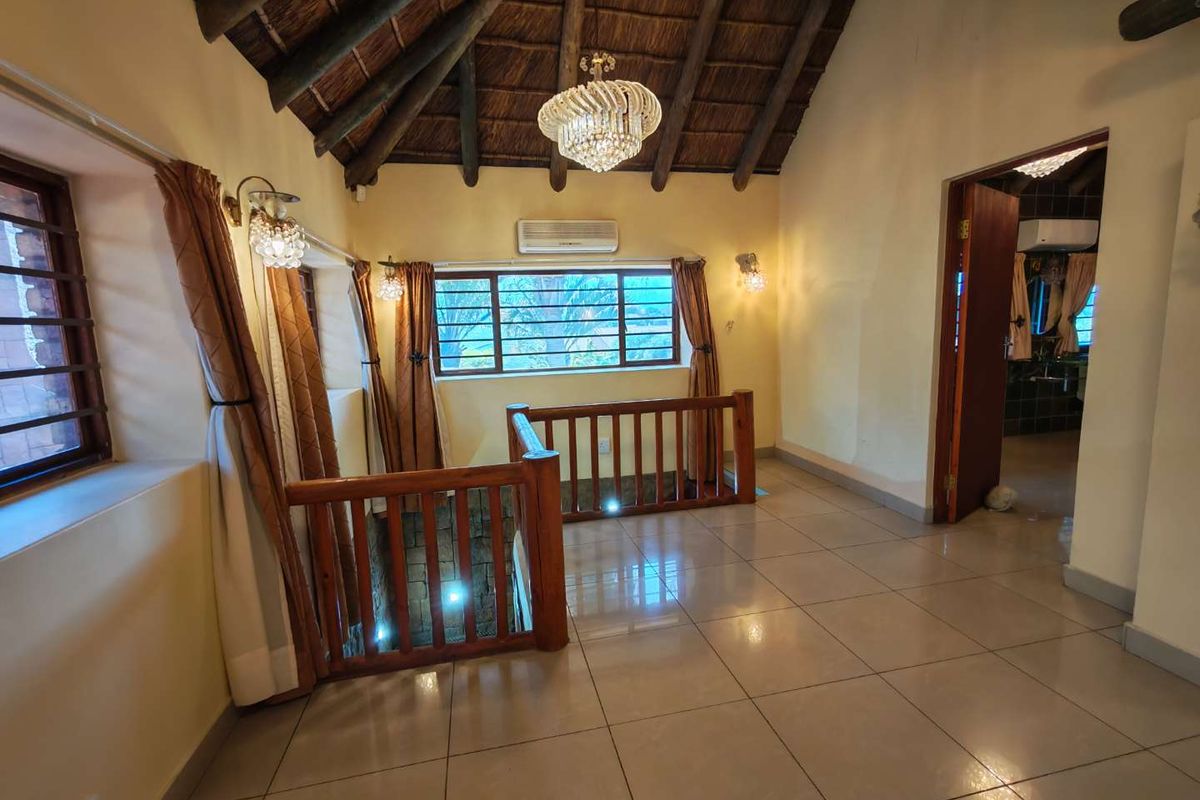 Spacious living area featuring a high vaulted thatched ceiling with exposed timber rafters, tiled flooring, and a timber balustrade overlooking the lower level.