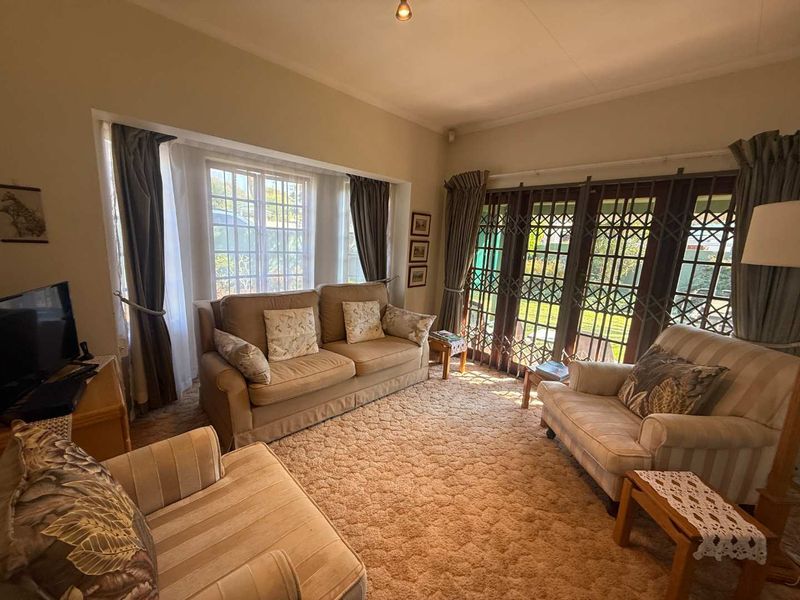 A comfortable living room featuring a large bay window, security gates, and direct access to the garden through classic french doors.