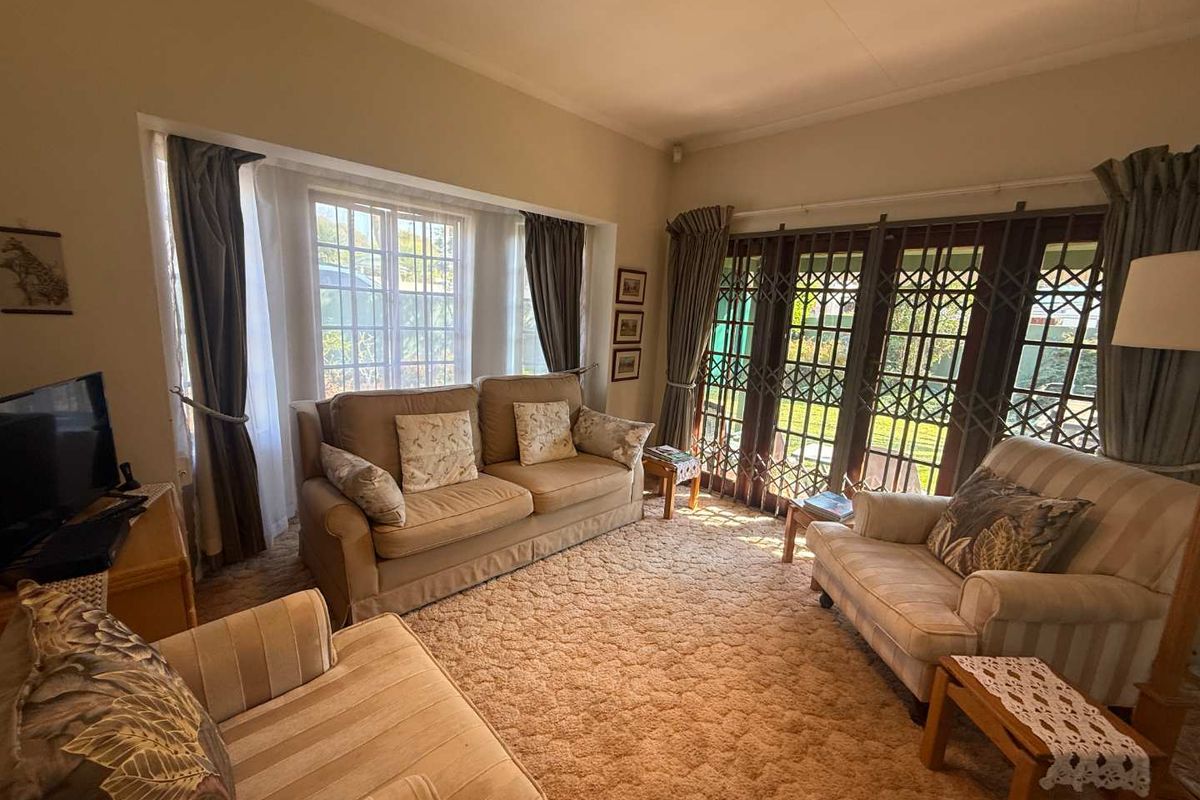 A comfortable living room featuring a large bay window, security gates, and direct access to the garden through classic french doors.